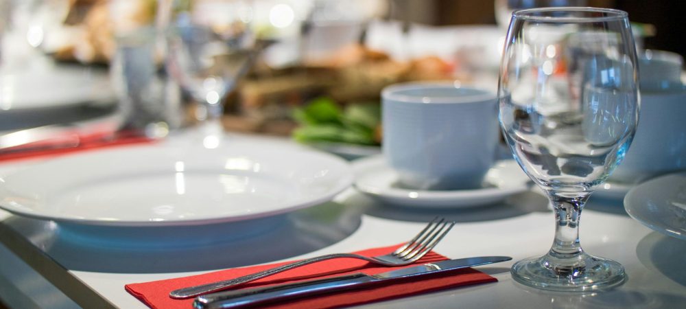 Close-up of an elegant dining table set with glassware, silverware, and red napkins in a restaurant setting.